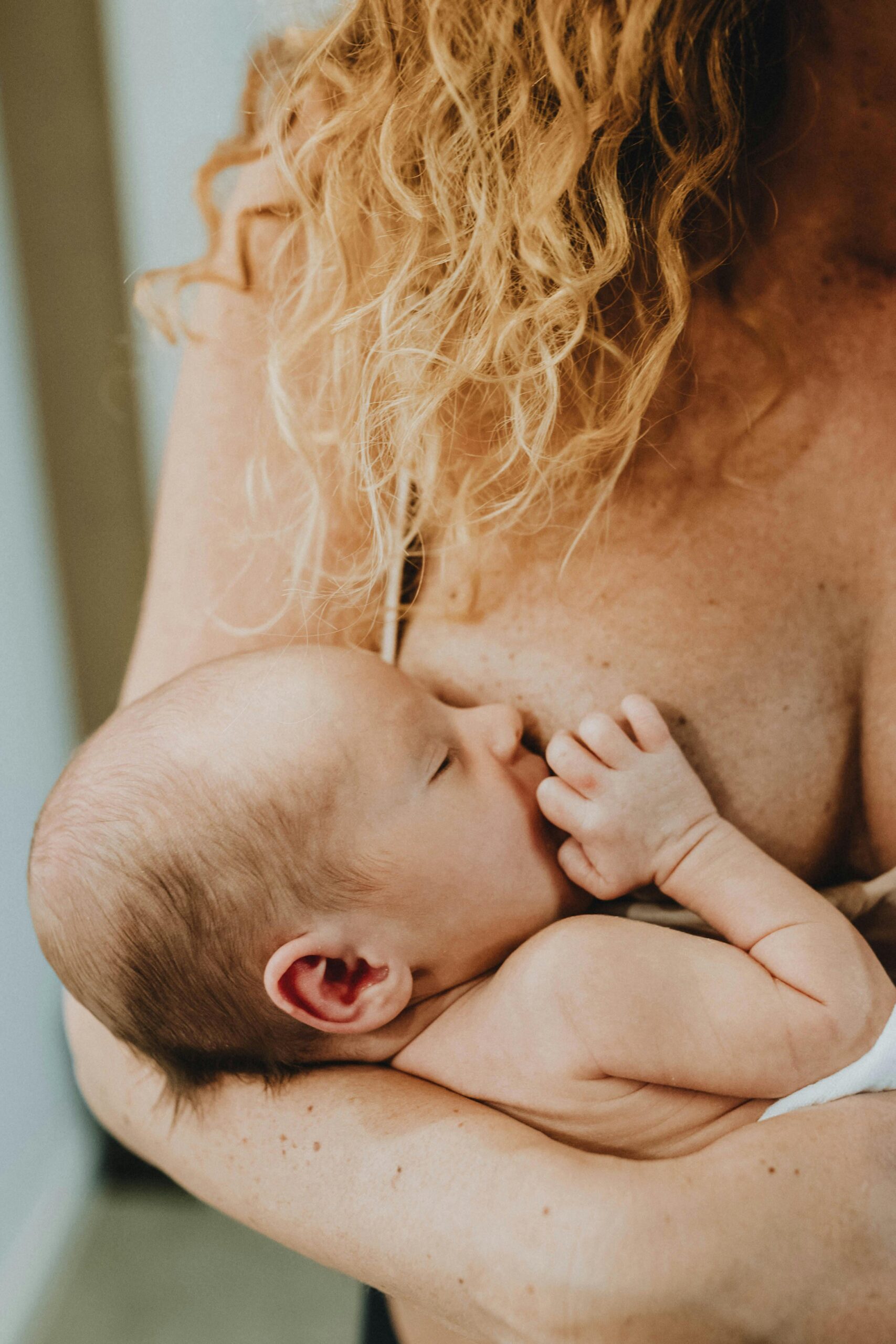 Tender moment of a mother breastfeeding her newborn baby in a cozy indoor setting.
